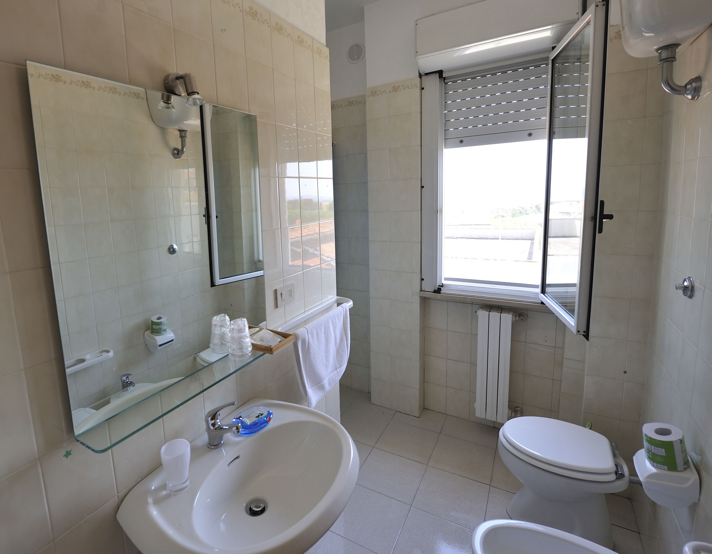 Une salle de bain avec un lavabo en verre, un miroir, des toilettes et une fenêtre avec des stores.