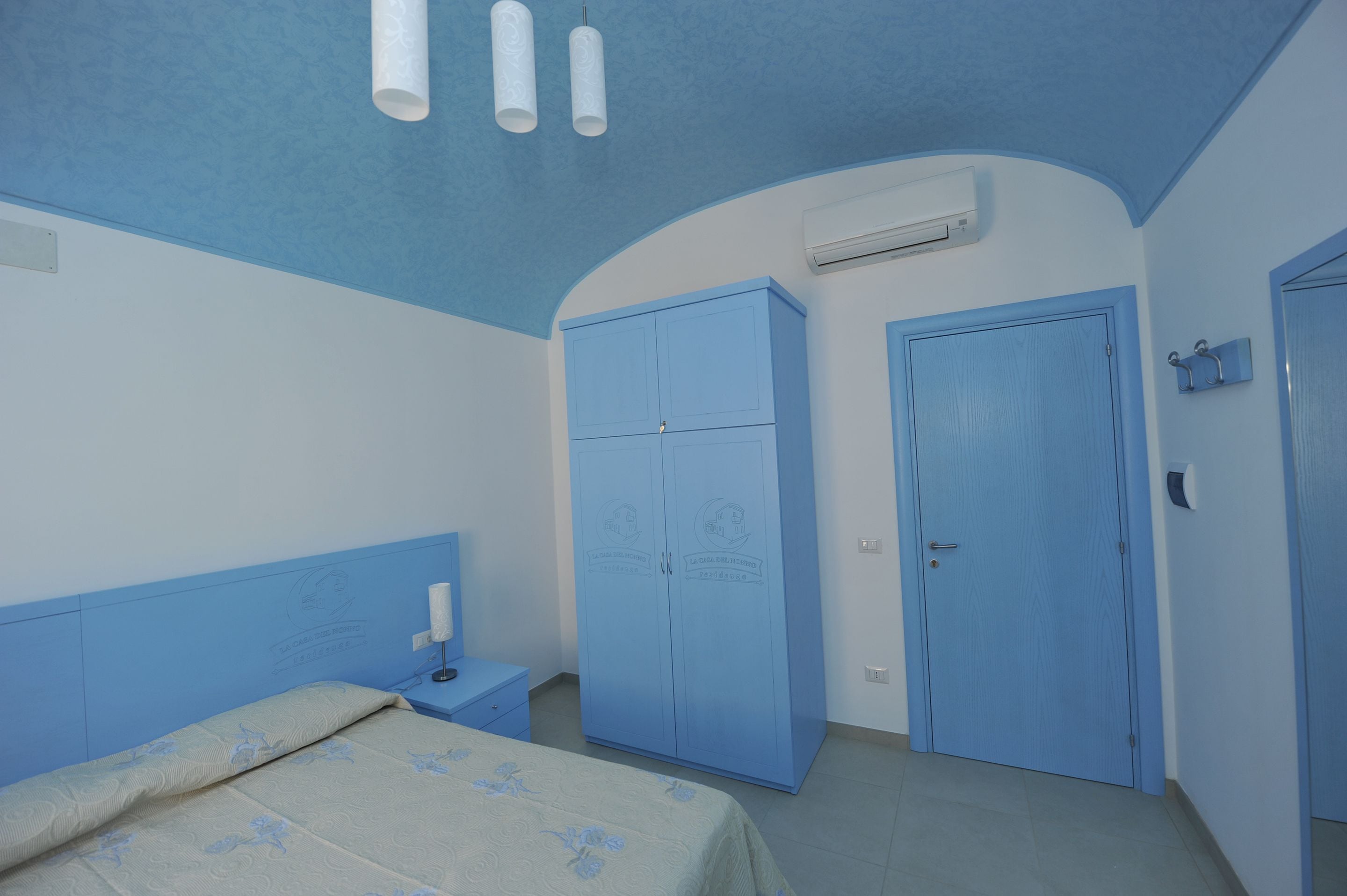 A bedroom with a bed, a wardrobe, a nightstand, and an air conditioning unit.