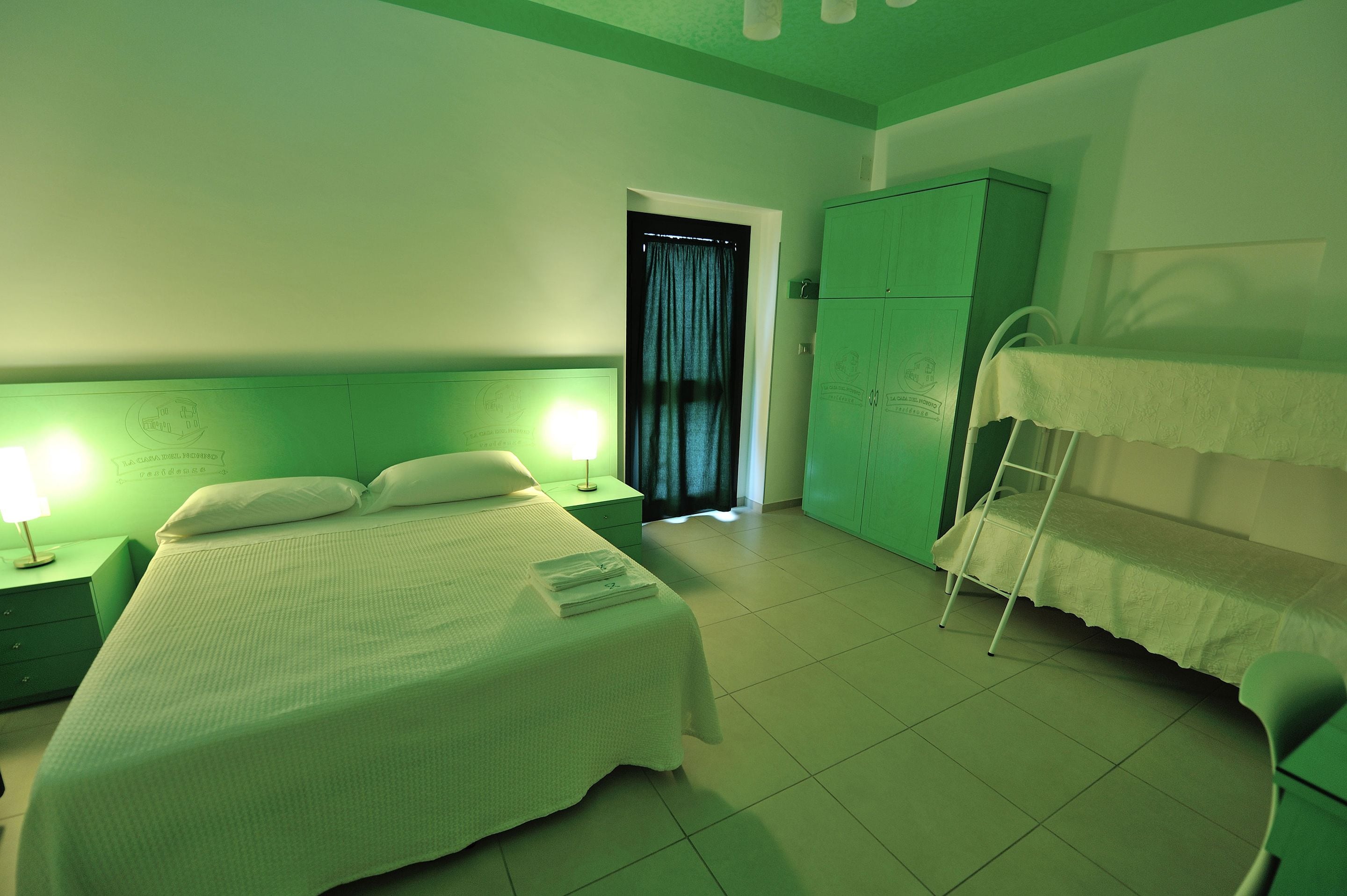 Una habitación con una cama, mesitas de noche, un armario y una litera.
