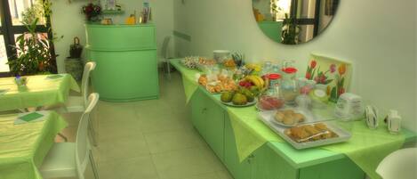 Un comedor con mesas y sillas verdes, un bufé con diversas opciones de comida y un espejo en la pared.
