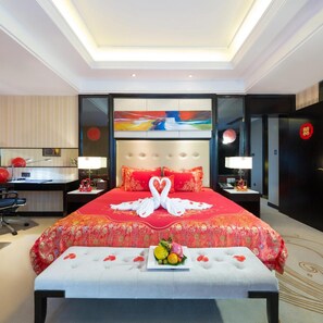 A hotel room with a large bed, a desk, and a chair. There is a painting on the wall and a red sign on the door. - Dading Century Plaza Hotel (Chengdu)