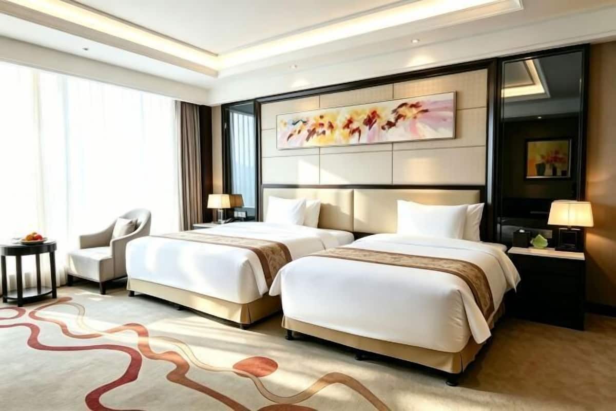 Habitación de hotel con dos camas, un escritorio, una silla y obras de arte en las paredes.