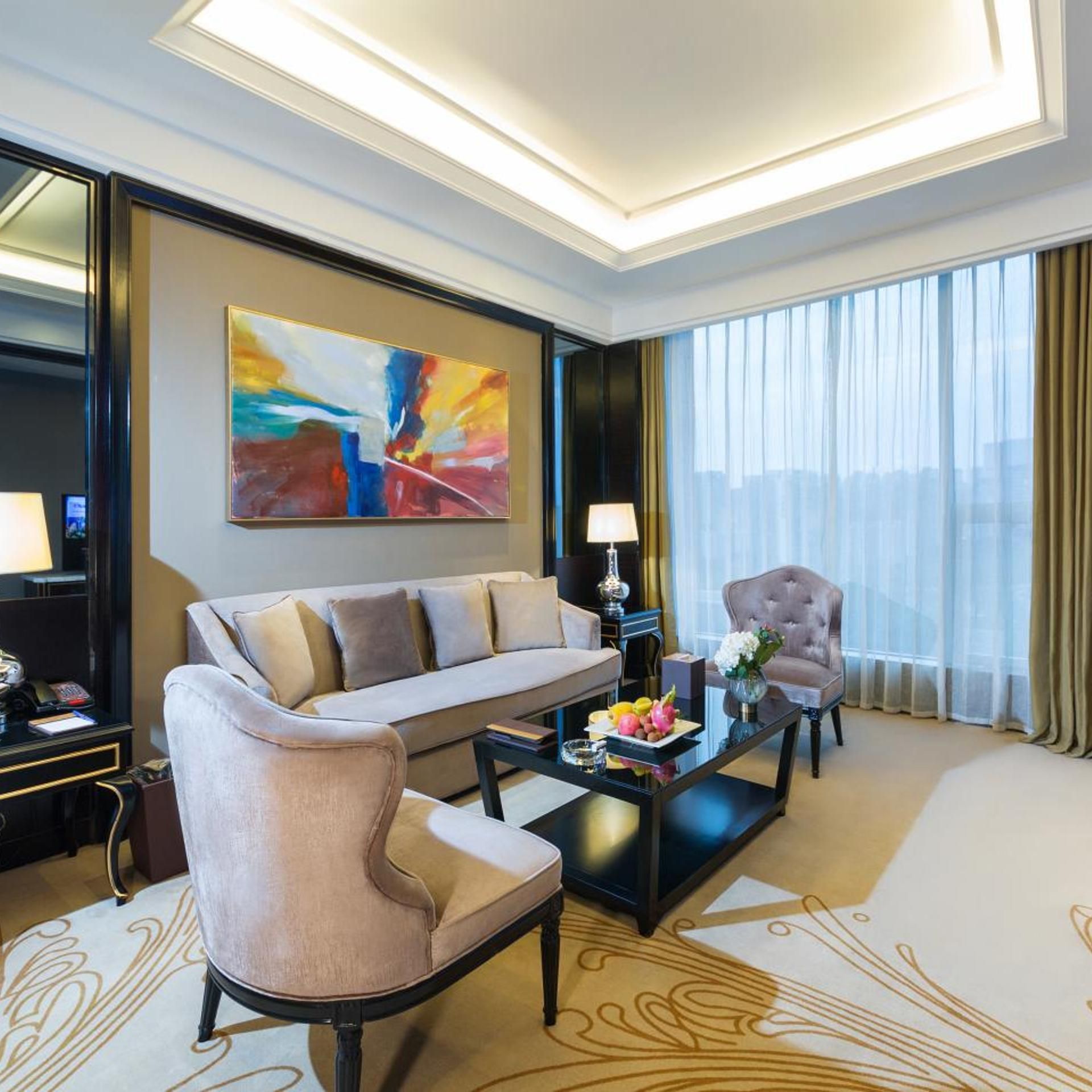 Habitación de hotel con sofá, sillón, mesa de centro y una obra de arte en la pared.