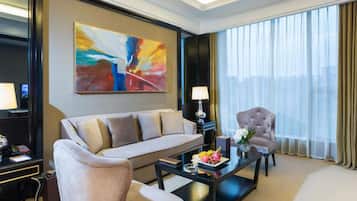 Habitación de hotel con sofá, sillón, mesa de centro y una obra de arte en la pared.