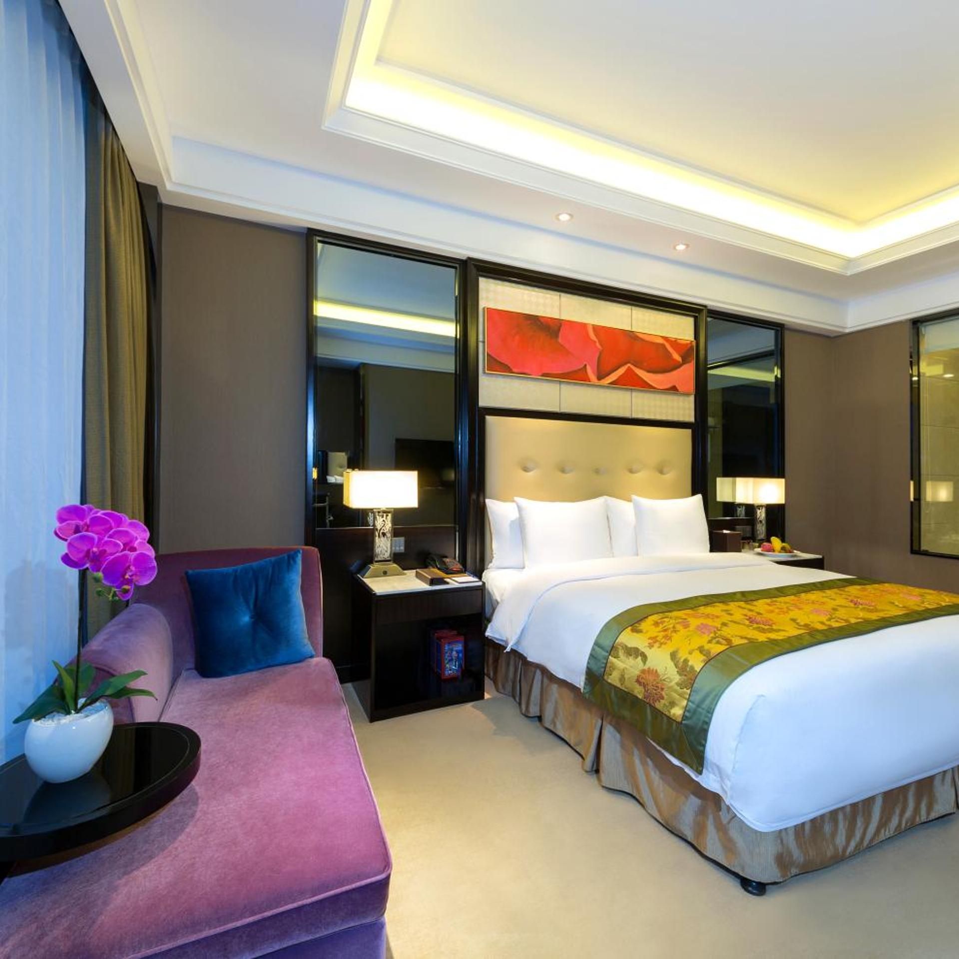 Een hotelkamer met een groot bed, een slaapbank, een nachtkastje, een lamp en een decoratieve spiegel.