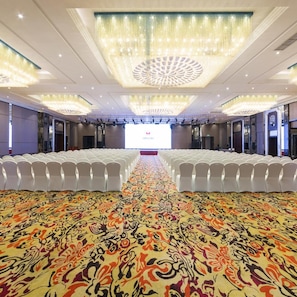 A conference room with rows of white chairs, a patterned carpet, and a large screen at the front. - Dading Century Plaza Hotel (Chengdu)