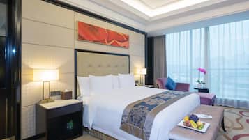 A hotel room with a large bed, bedside tables, a desk, and a view of the city through large windows.