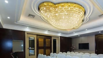 A conference room with rows of white chairs, a large chandelier, and a patterned carpet.