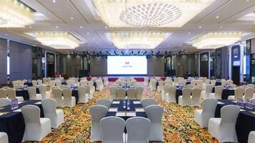 A conference room with rows of tables and chairs, a large screen at the front, and a patterned carpet.