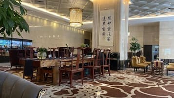A hotel lobby with a central dining area, a reception desk, and a large pillar with text.
