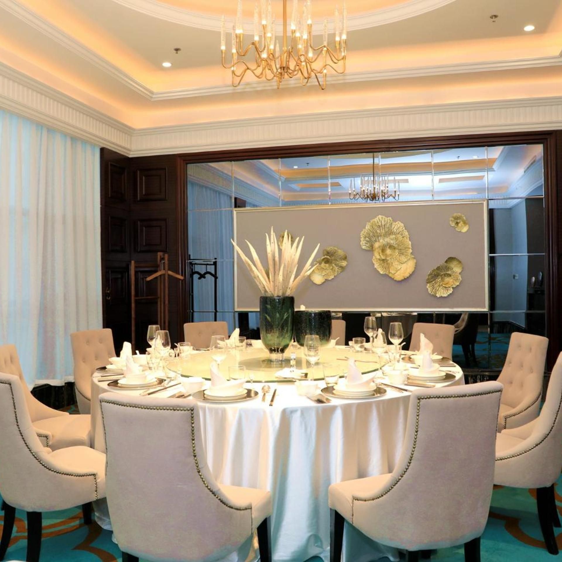 A formal dining room with a round table set for a meal, surrounded by upholstered chairs.