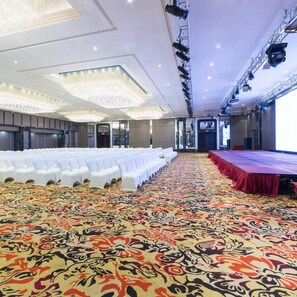 A conference room with rows of white chairs, a stage with a red backdrop, and a patterned carpet. - Dading Century Plaza Hotel (Chengdu)