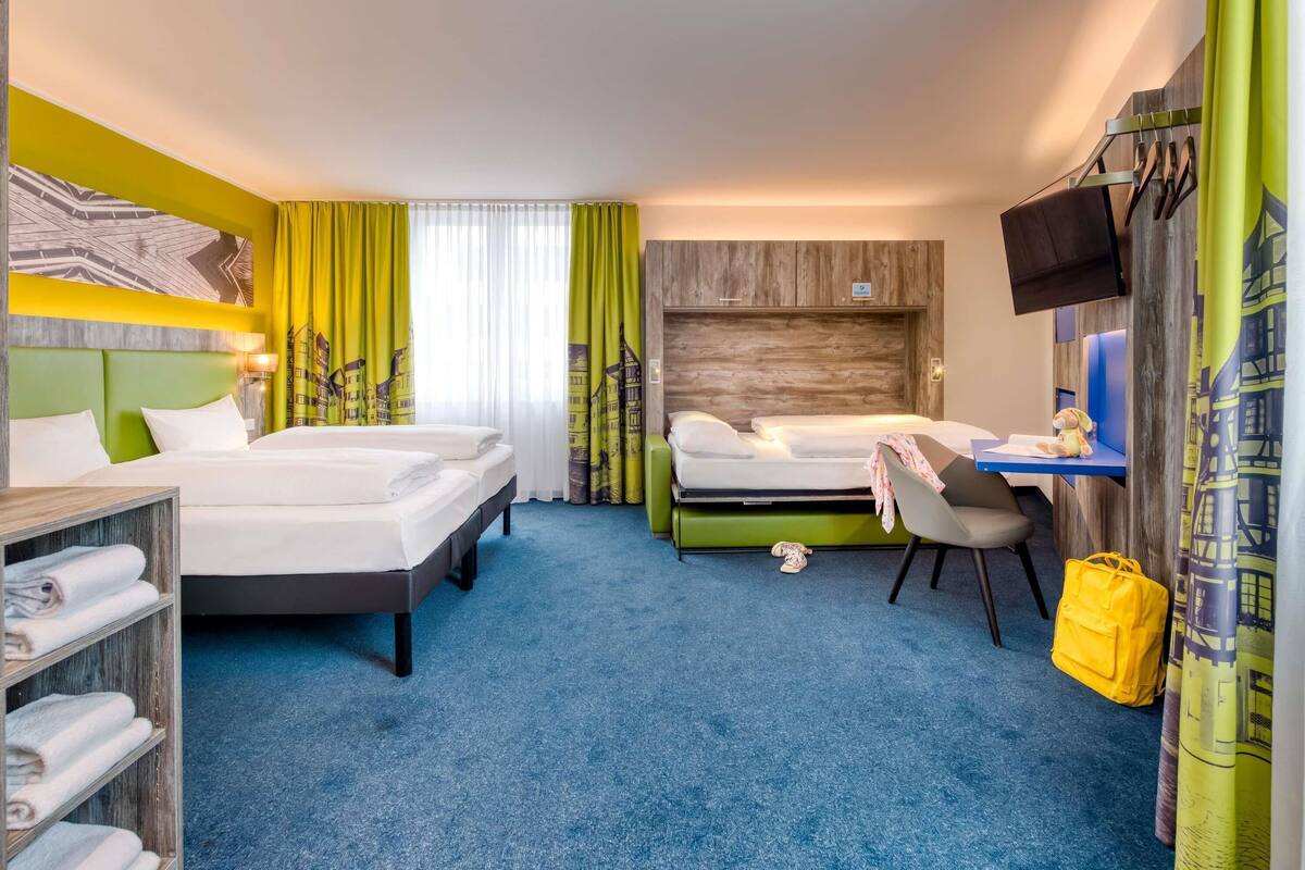 A hotel room with two beds, a desk, a chair, a TV, and a wardrobe.