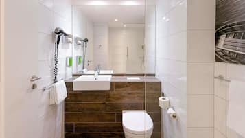 Un baño moderno con inodoro blanco, dos lavamanos, secador de pelo y ducha.