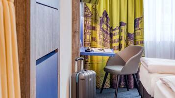 A hotel room with a bed, a desk, a chair, and a suitcase.