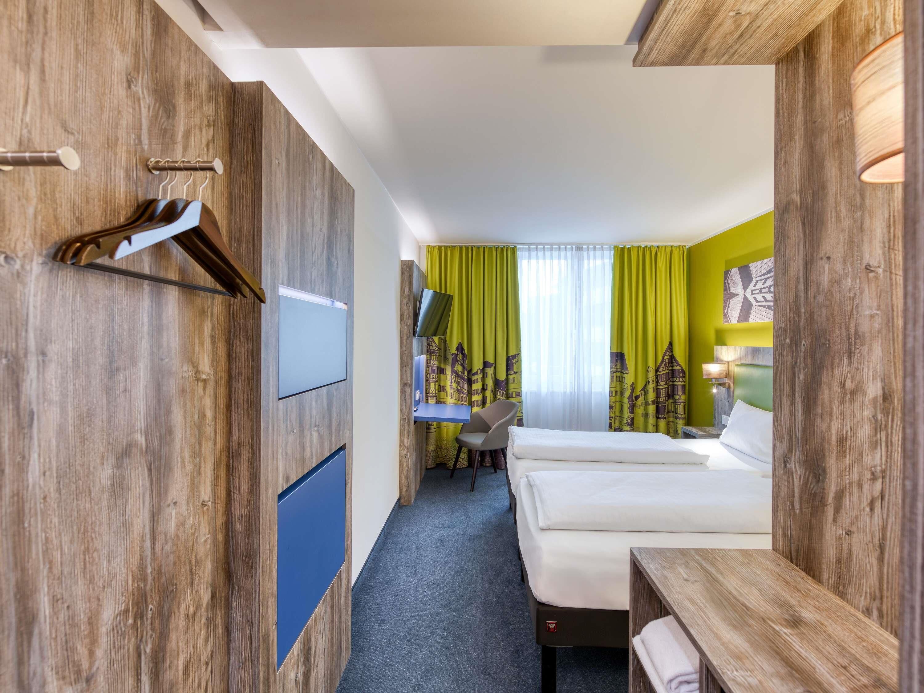 A hotel room with a bed, desk, and chair, wooden walls, and a green curtain.