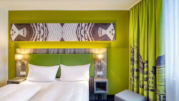 A hotel room with a large bed, two bedside tables, a headboard with a geometric pattern, and a view of a cityscape through curtains.