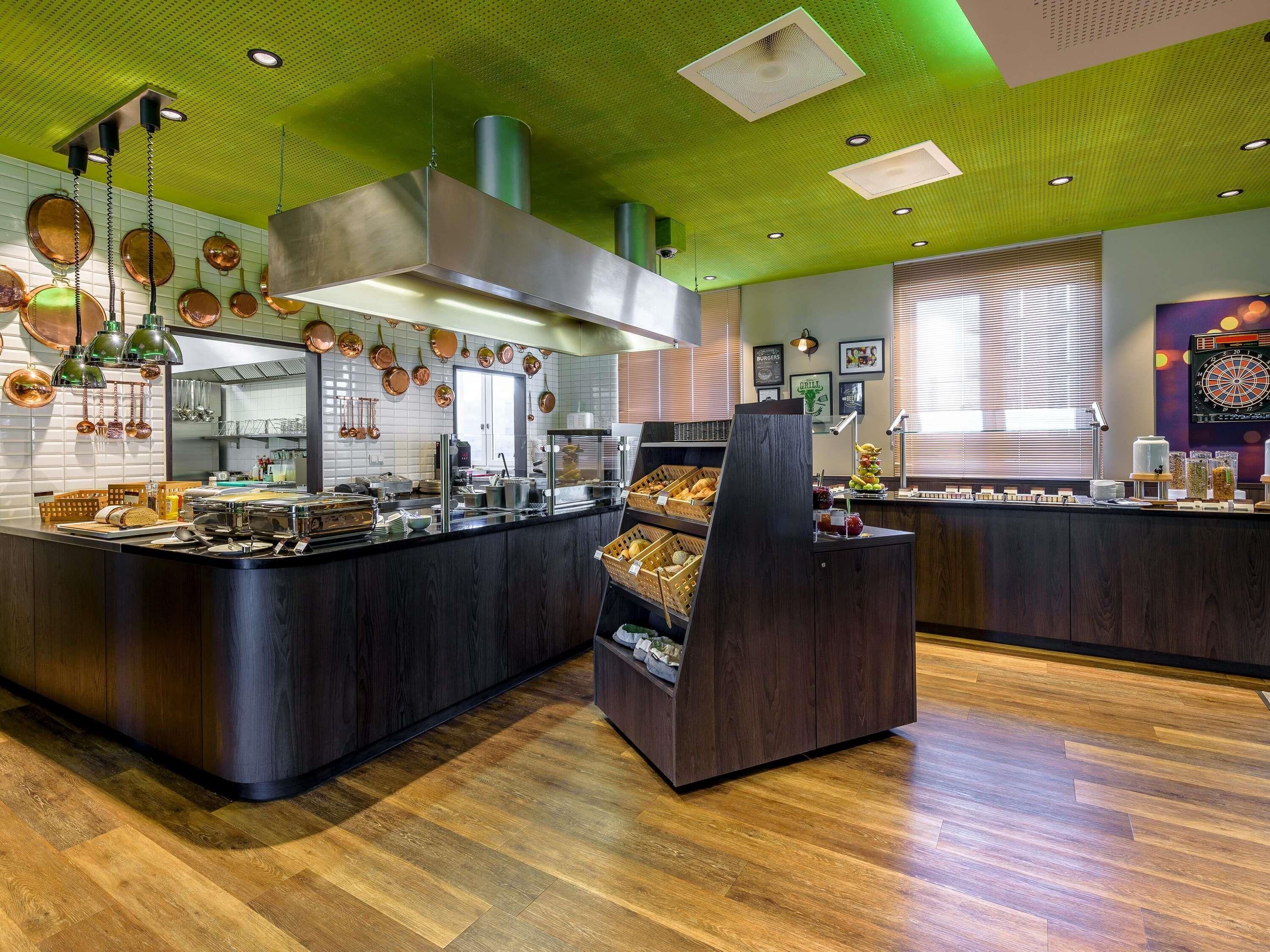 A modern kitchen with a central island, overhead ventilation, and a dartboard on the wall.