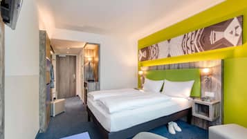 A hotel room with a large bed, a desk, a chair, and a wardrobe.