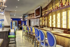 A bar area with a long counter, multiple bar stools, and shelves with bottles and glasses. - ibis Styles Rastatt Baden Baden (Rastatt)