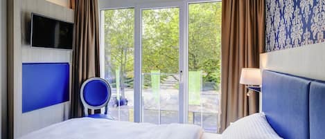 Habitación de hotel con cama, televisión, una silla y vistas al exterior.