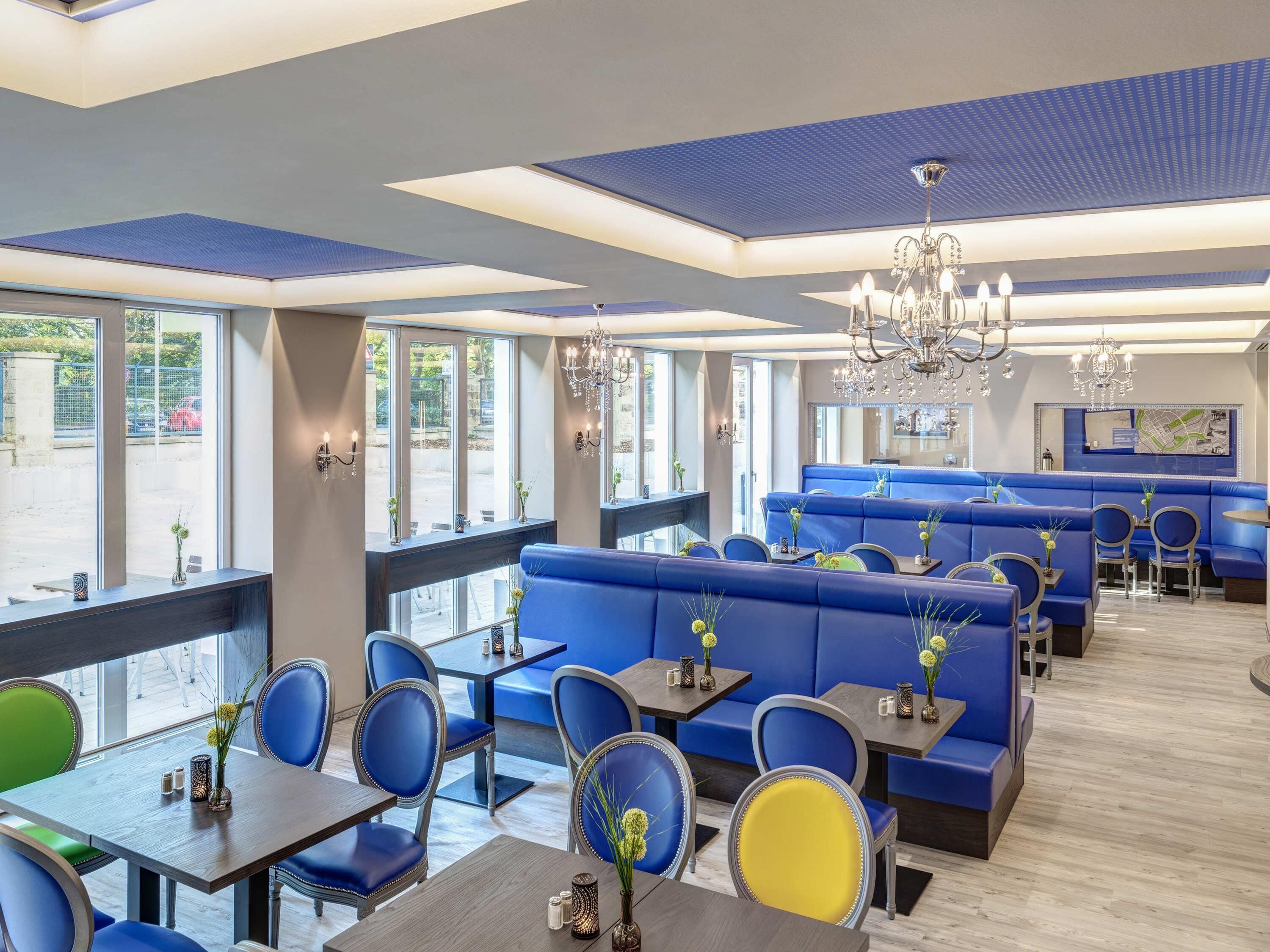 A restaurant with blue seating, large windows, chandeliers, and a map on the wall.