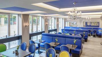 A restaurant with blue seating, large windows, chandeliers, and a map on the wall.