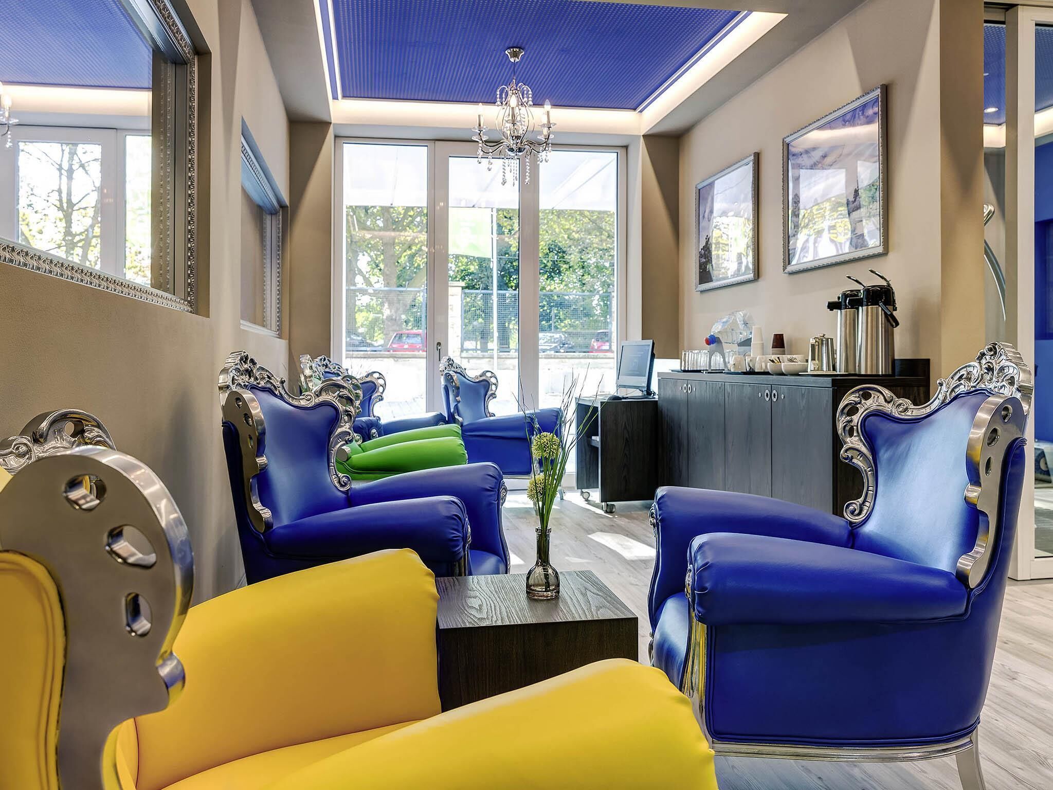 Ein Zimmer mit blauen und gelben Stühlen, einem Schreibtisch und einer Chandelüster.