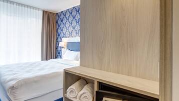 Habitación de hotel con cama, lámpara de pared, microondas integrado y alfombra azul estampada.