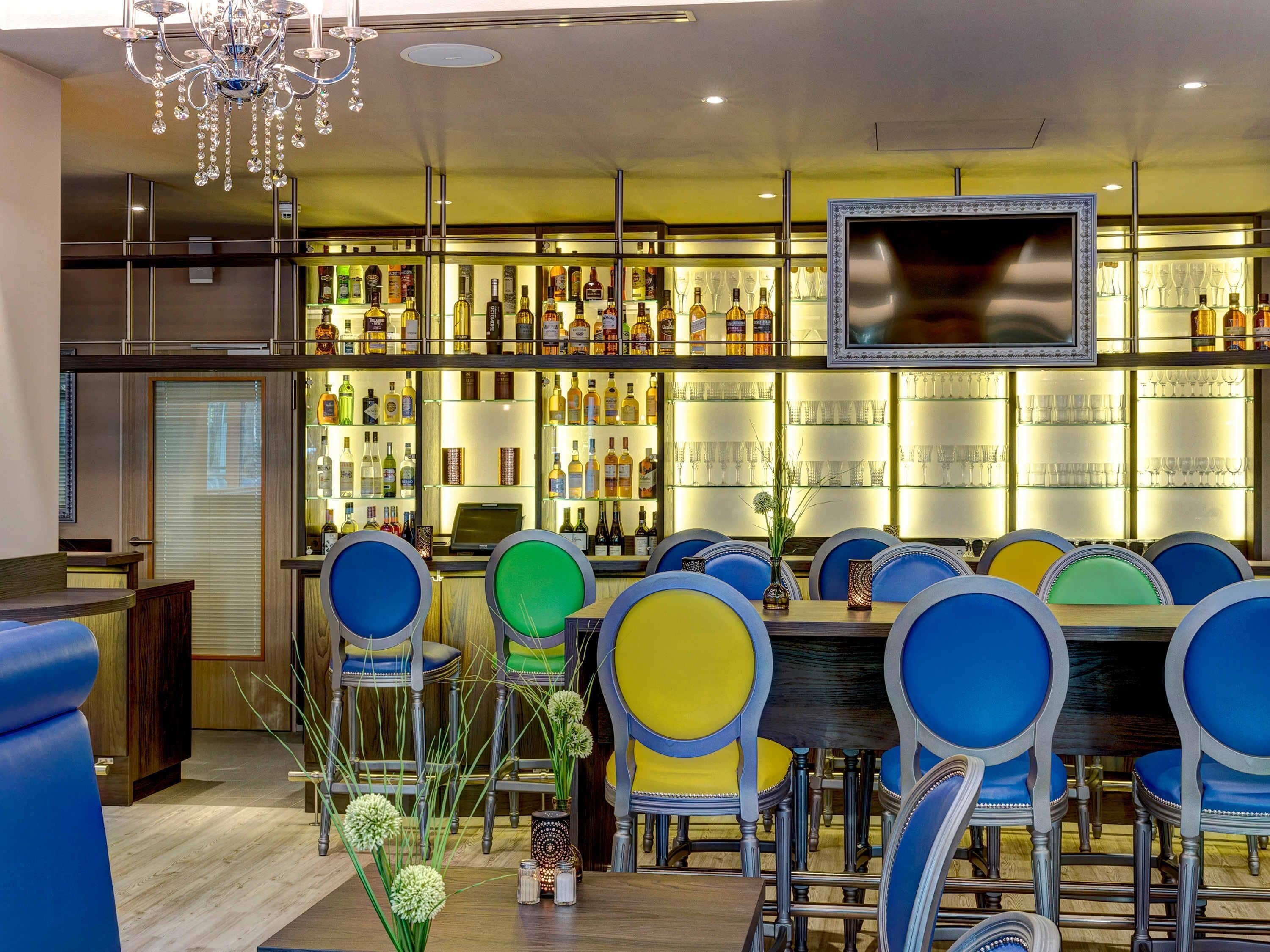 A bar area with a TV, multiple liquor bottles, and colorful bar stools.