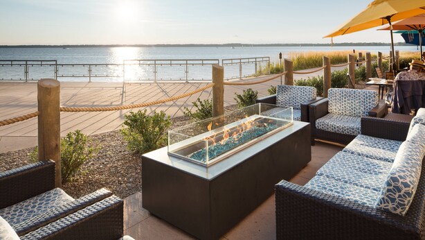 Un área de estar al aire libre con mobiliario de mimbre, un elemento decorativo con fuego de vidrio y vistas al agua.