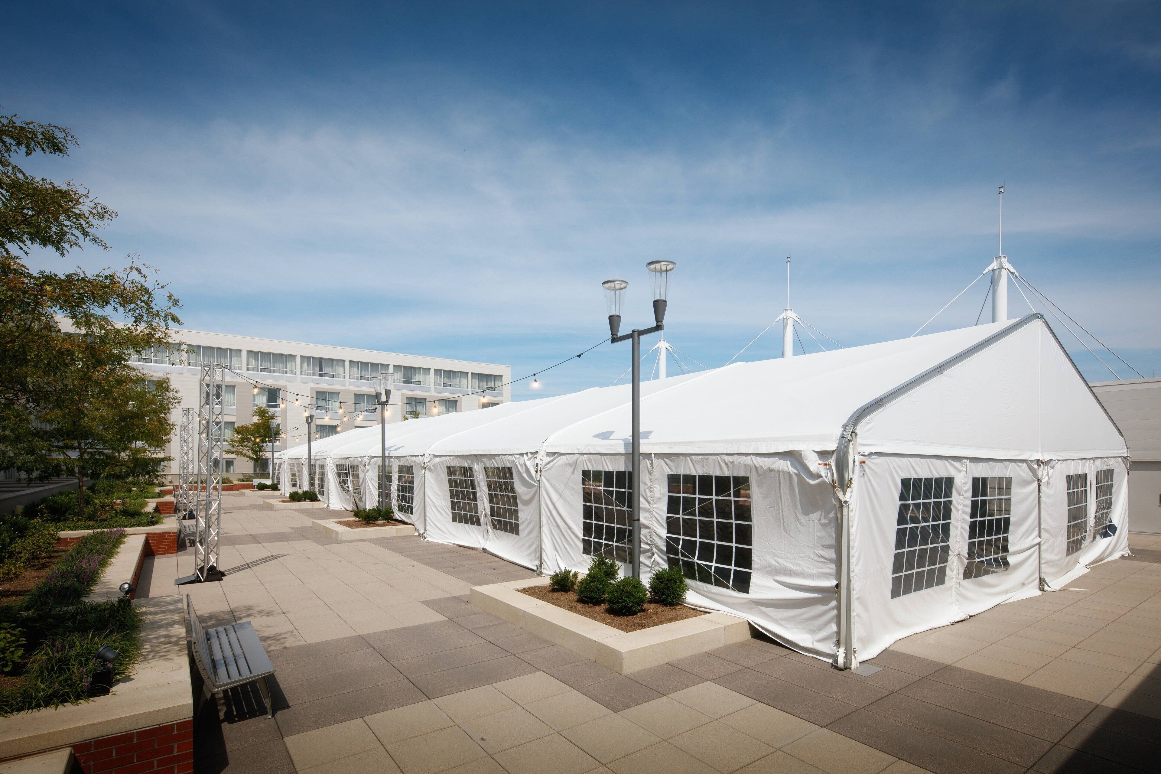 A row of white tents with windows, a paved walkway, and a building in the background.