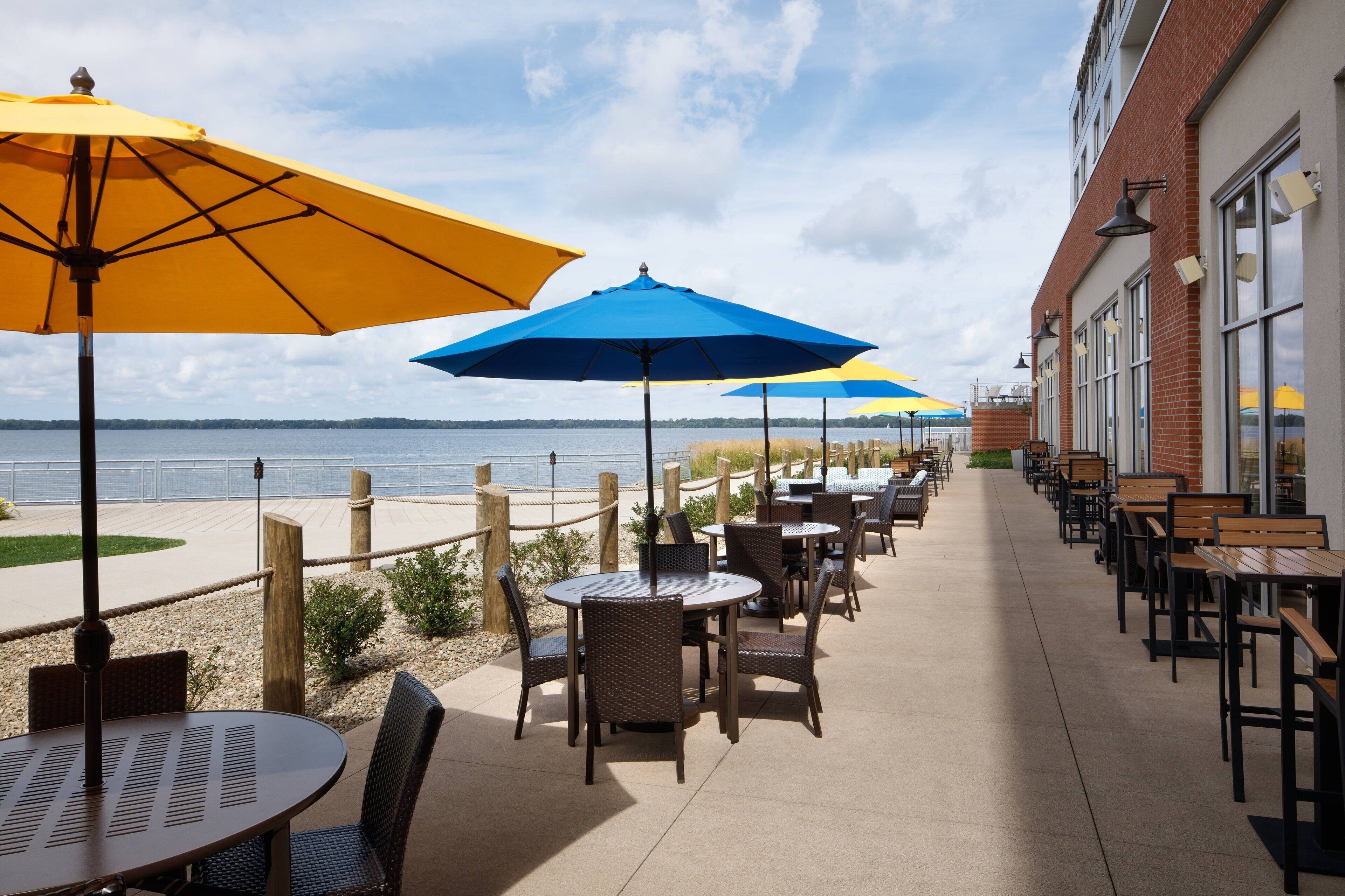 An outdoor patio with tables and chairs, umbrellas, and a view of the water.