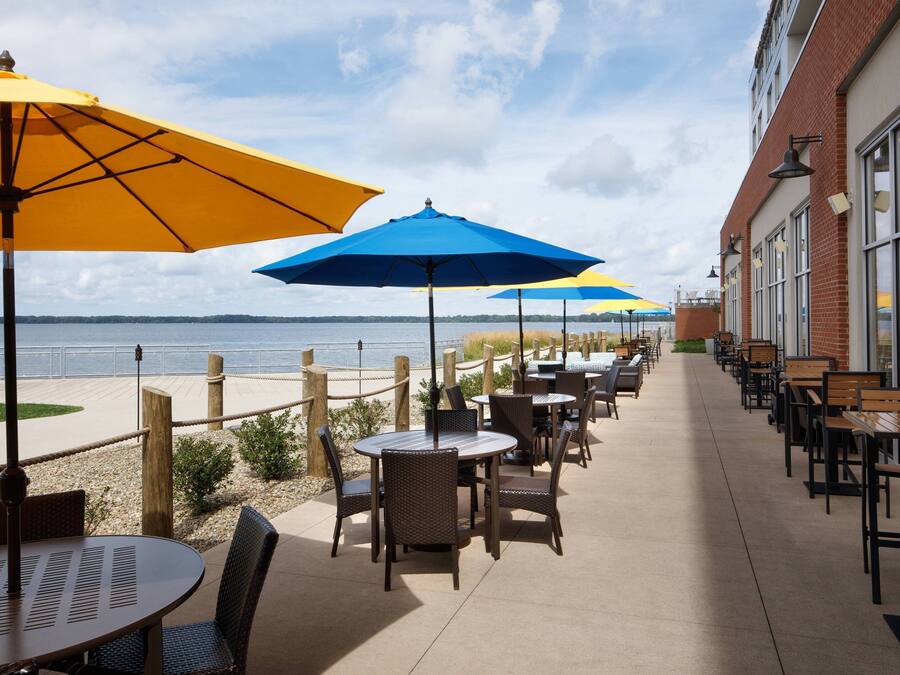 An outdoor patio with tables and chairs, umbrellas, and a view of the water.