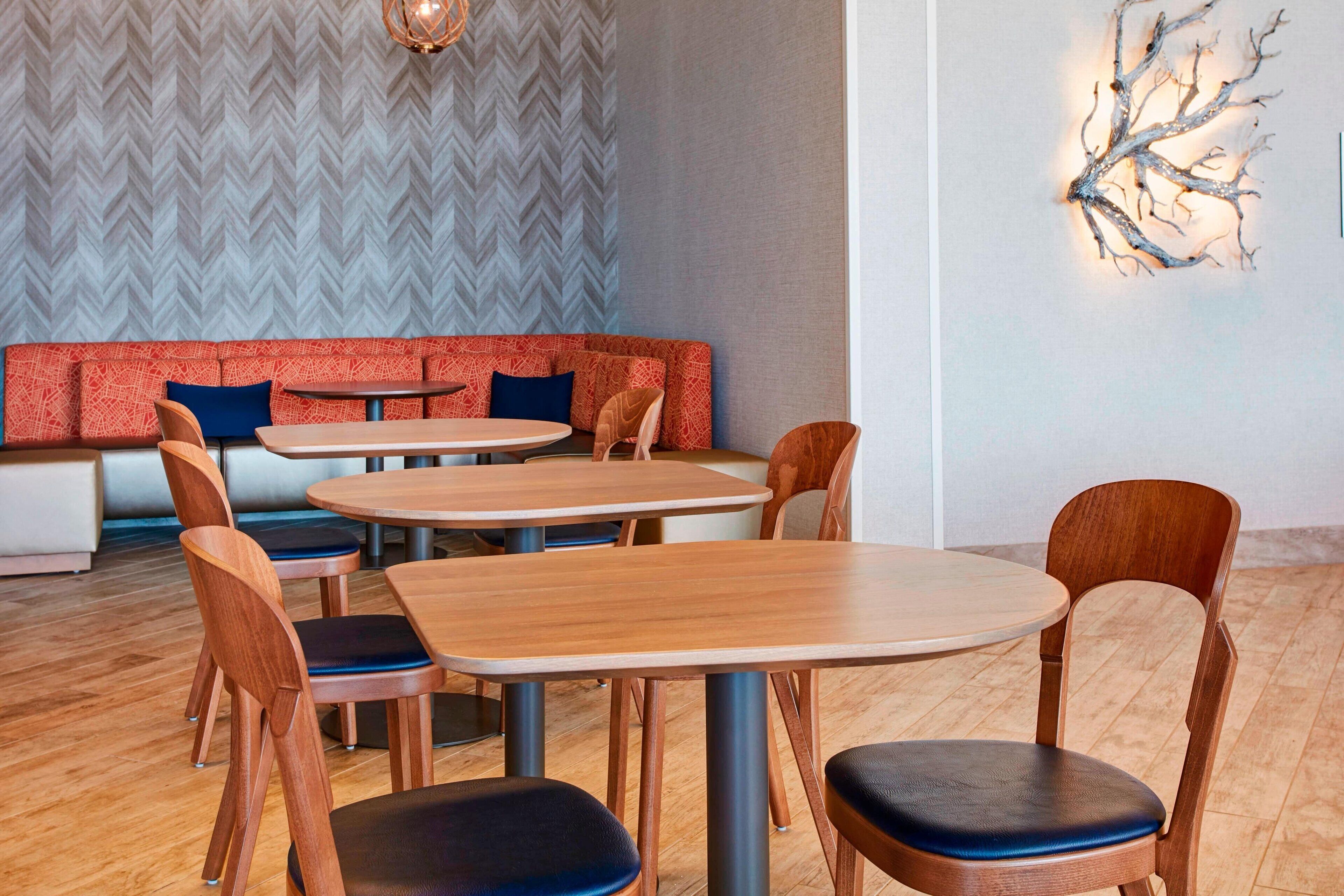A modern dining area with wooden tables and chairs, a red cushioned bench, and a decorative wall piece.