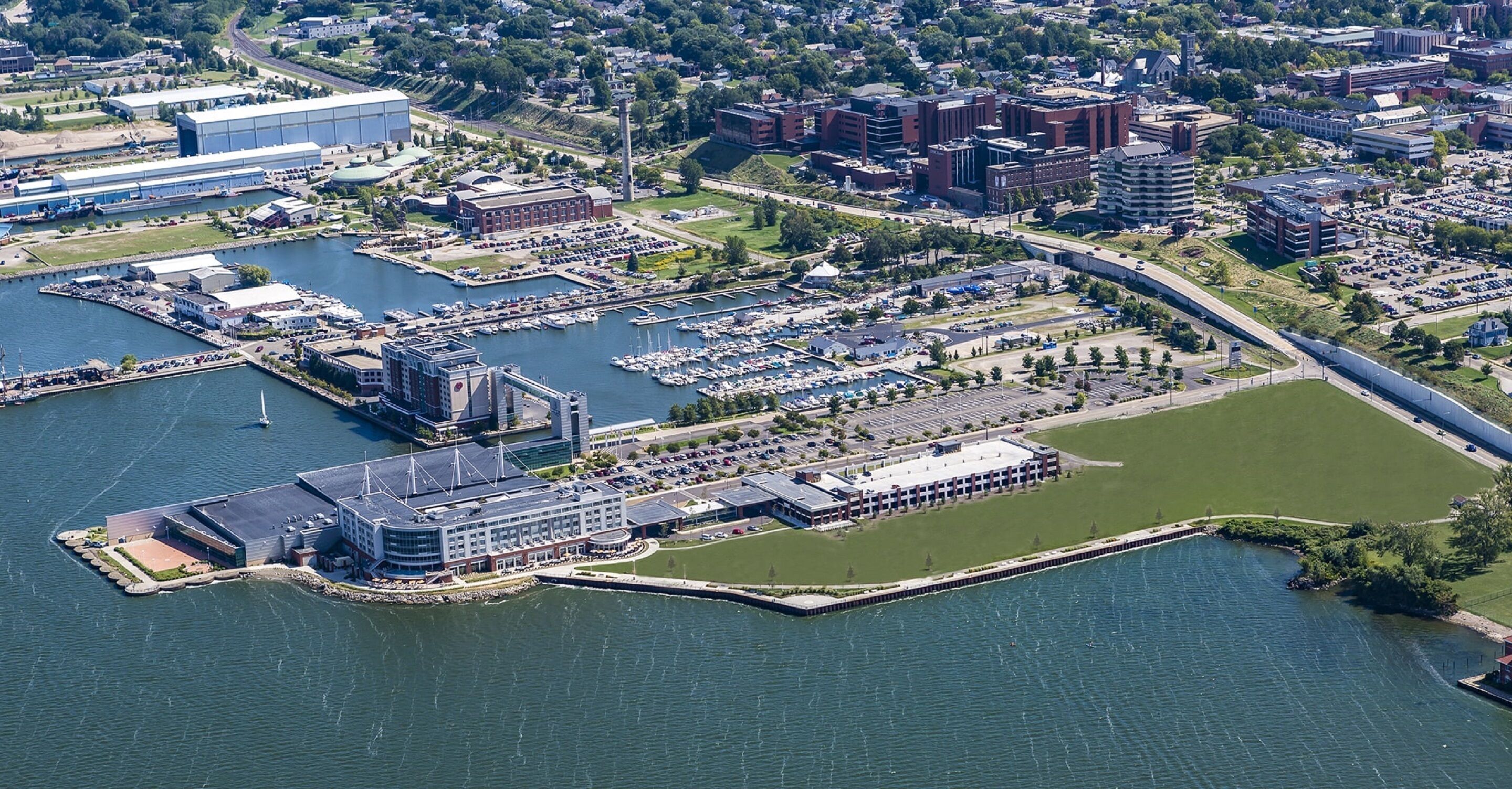 An aerial view of a marina with boats, a large building with a glass facade, and a bridge connecting to the land.