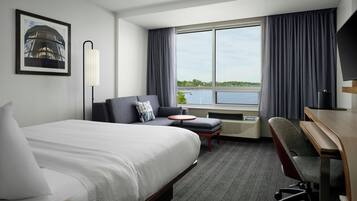 A hotel room with a bed, a sofa, a desk, a chair, a TV, a window with curtains, and a picture on the wall.