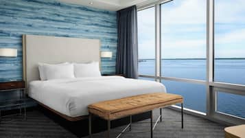 A hotel room with a large bed, a bench, a nightstand, and a view of the water.