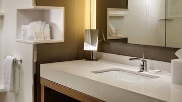 A modern bathroom with a white sink, a mirror, and a shelf with toiletries.