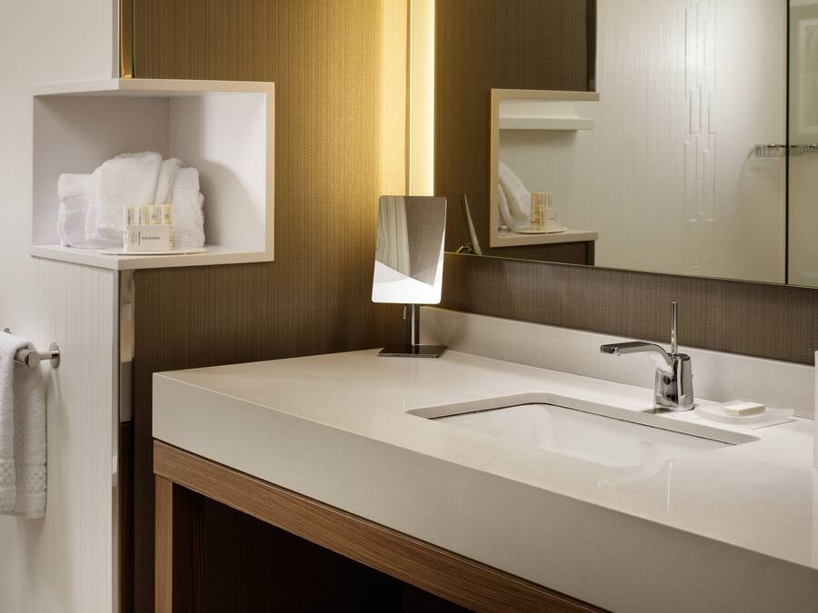 A modern bathroom with a white sink, a mirror, and a shelf with toiletries.