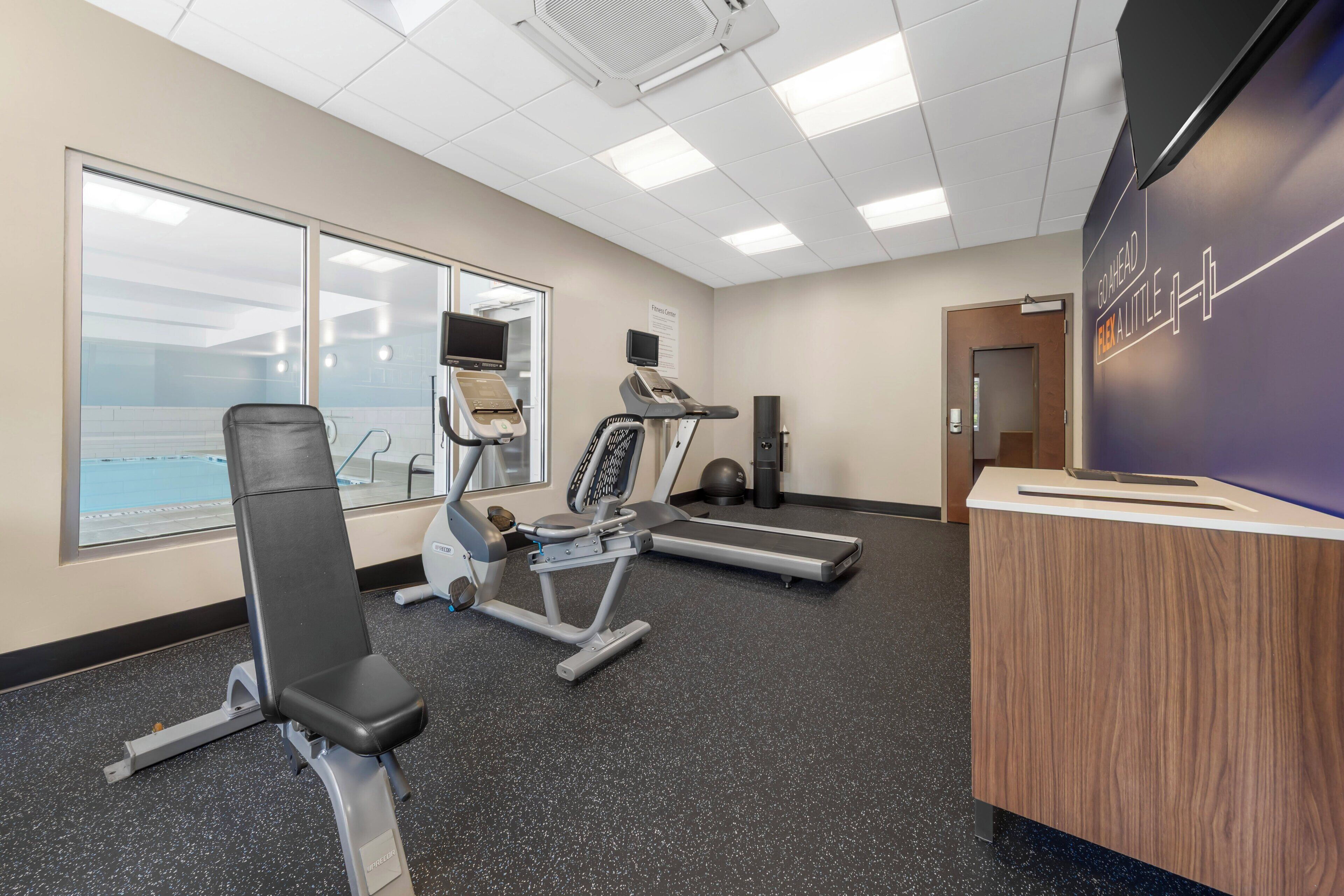 A fitness center with cardio equipment, a reception desk, and a large window.