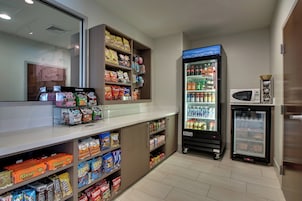 Un bar de aperitivos con una variedad de snacks y bebidas envasadas, incluyendo un refrigerador y un microondas.