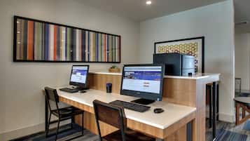 A hotel room with a desk, two computers, a chair, and a decorative wall piece.