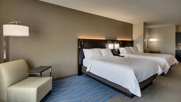 A hotel room with two beds, a sofa, a desk, and a lamp.