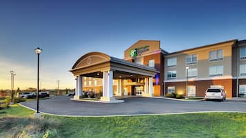 Et Holiday Inn Express hotel med et overdækket indgangsparti, parkeringsplads og en klar himmel.