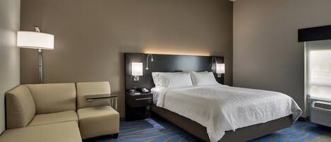 A hotel room with a bed, a sofa, a nightstand, a lamp, and a window.