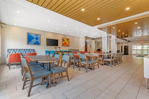 Amplio espacio interior con diversas disposiciones de asientos, incluidas mesas y sillas, y un techo alto con paneles de madera.