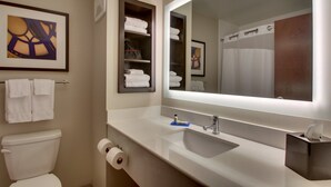 Een badkamer met een wit wastafel, spiegel en toilet. Handdoeken liggen op een rek en er hangt een afbeelding in een lijst aan de muur.