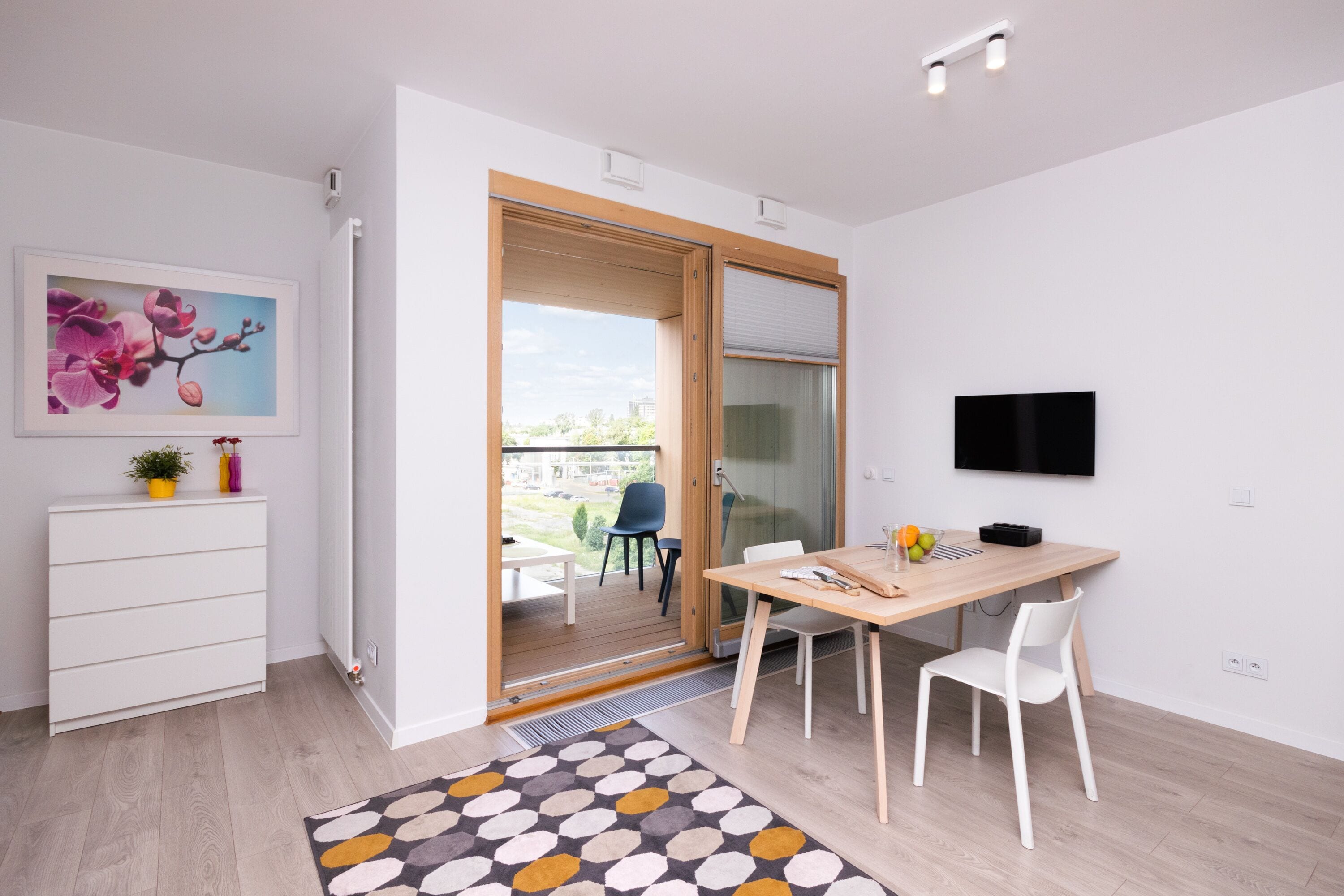 Une cuisine moderne avec une table en bois, des chaises blanches et un téléviseur fixé au mur.