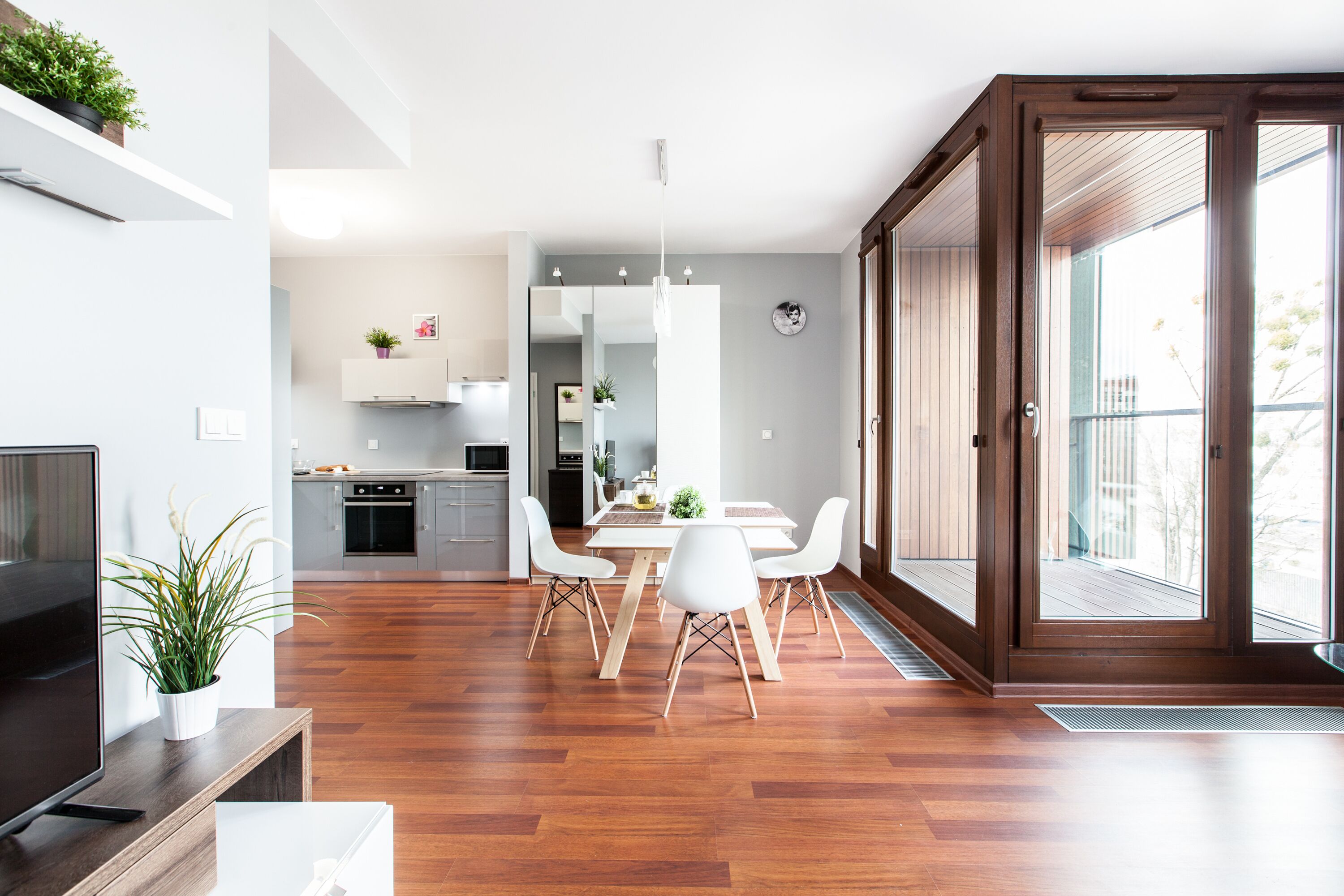 Una cocina moderna con armarios blancos, un comedor con una mesa y sillas blancas, y un amplio ventanal corredero al exterior.